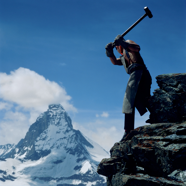 Shirtless man hammering on a snowy mountain