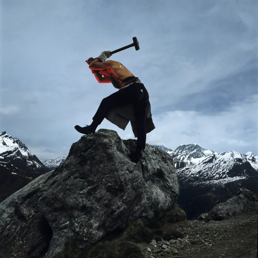 Shirtless man hammering on a mountain